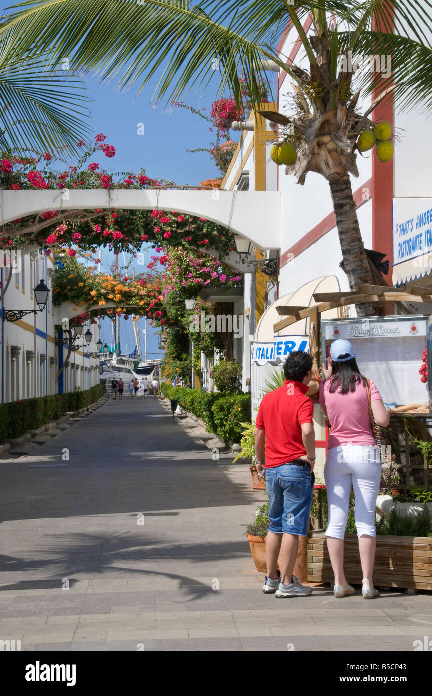 Picturesque walkway with Bougainvillea and tourists reading restaurant menu in Puerto de Mogan Gran Canaria Canary Islands Spain Stock Photo