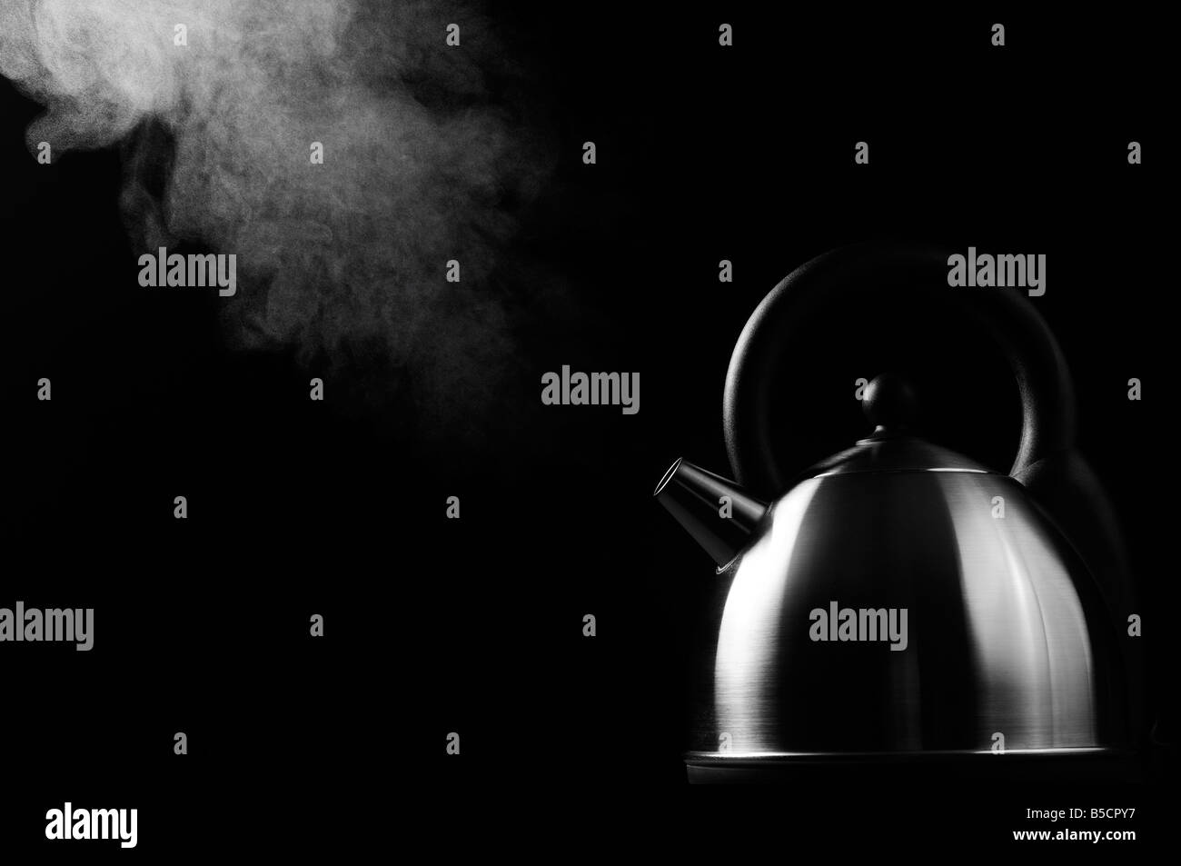 Boiling kettle on black background with steam rising to the light Stock Photo
