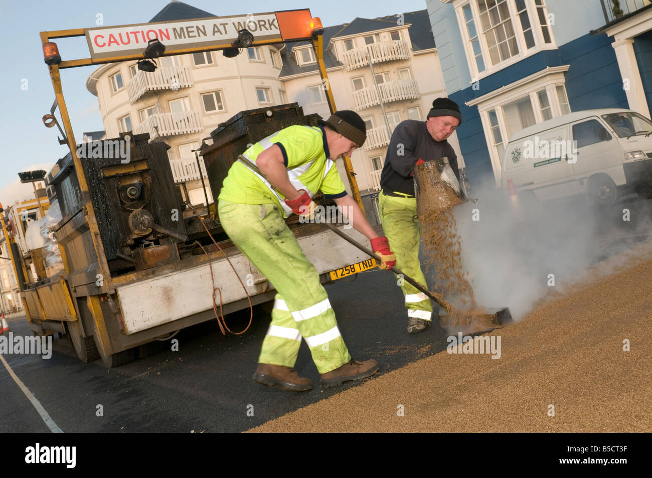 Two men laying high friction anti skid resistant road surface 'caution men at work', Aberystwyth Wales UK Stock Photo
