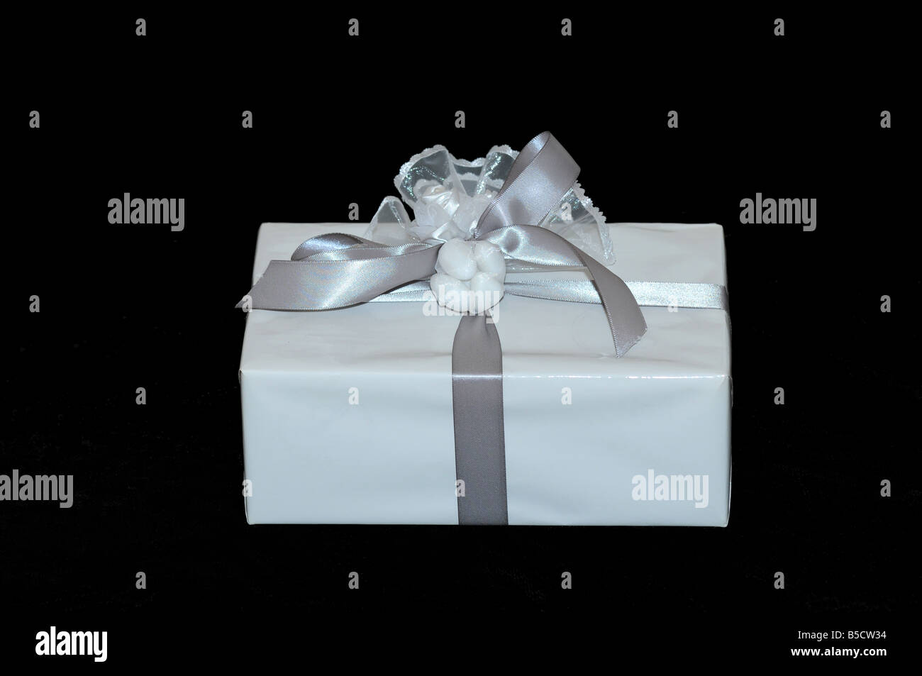 white gift box with silver ribbon on black background an engagement party favor adorned with a apcket of jordan almonds Stock Photo