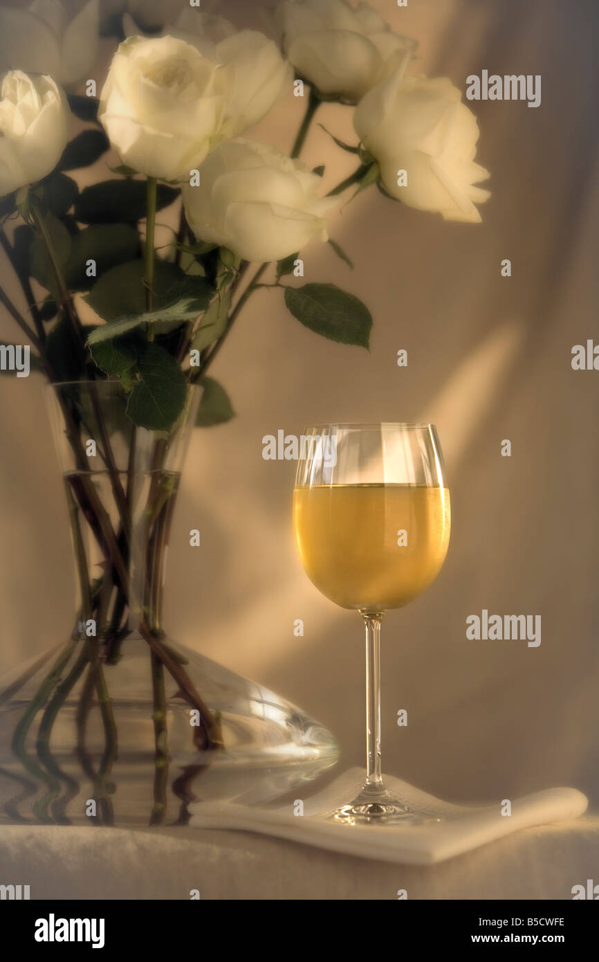 white roses in a vase with a glass of white wine Stock Photo