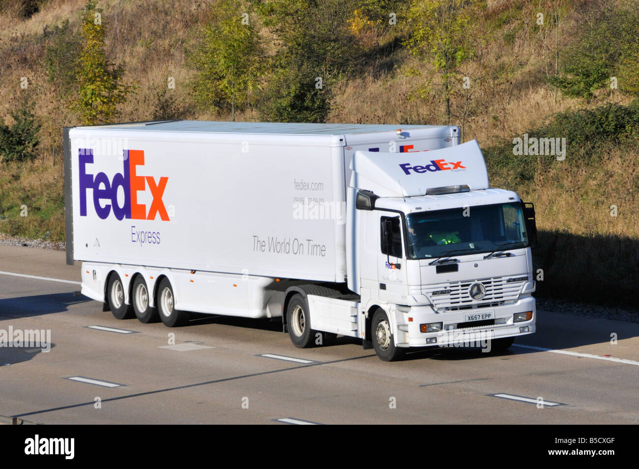 Side front view white FedEx UK brand delivery service business hgv transport lorry truck driver and articulated trailer driving on M25 motorway road Stock Photo