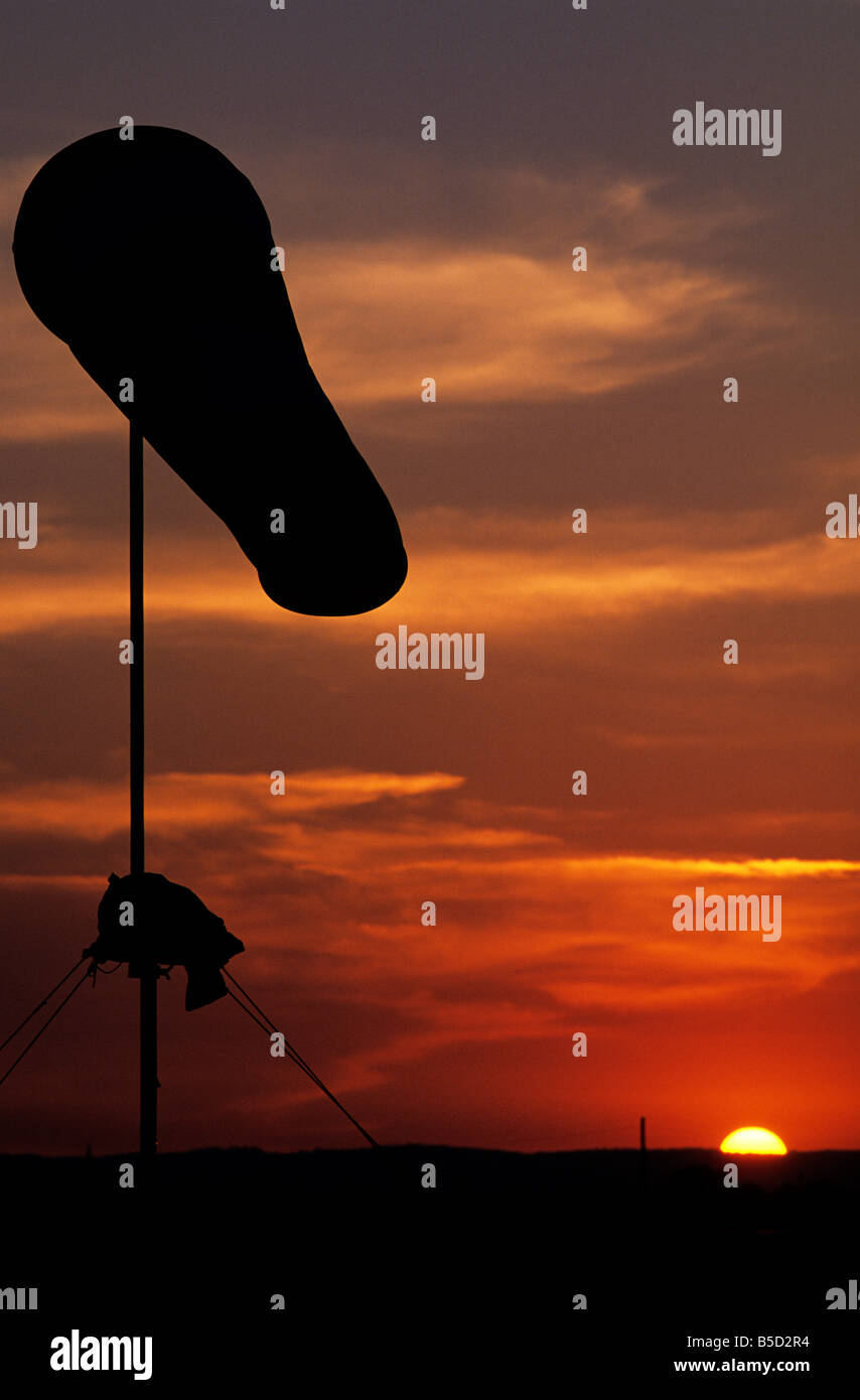 A wind sock, or wind cone, silhouetted against the setting sun. Stock Photo