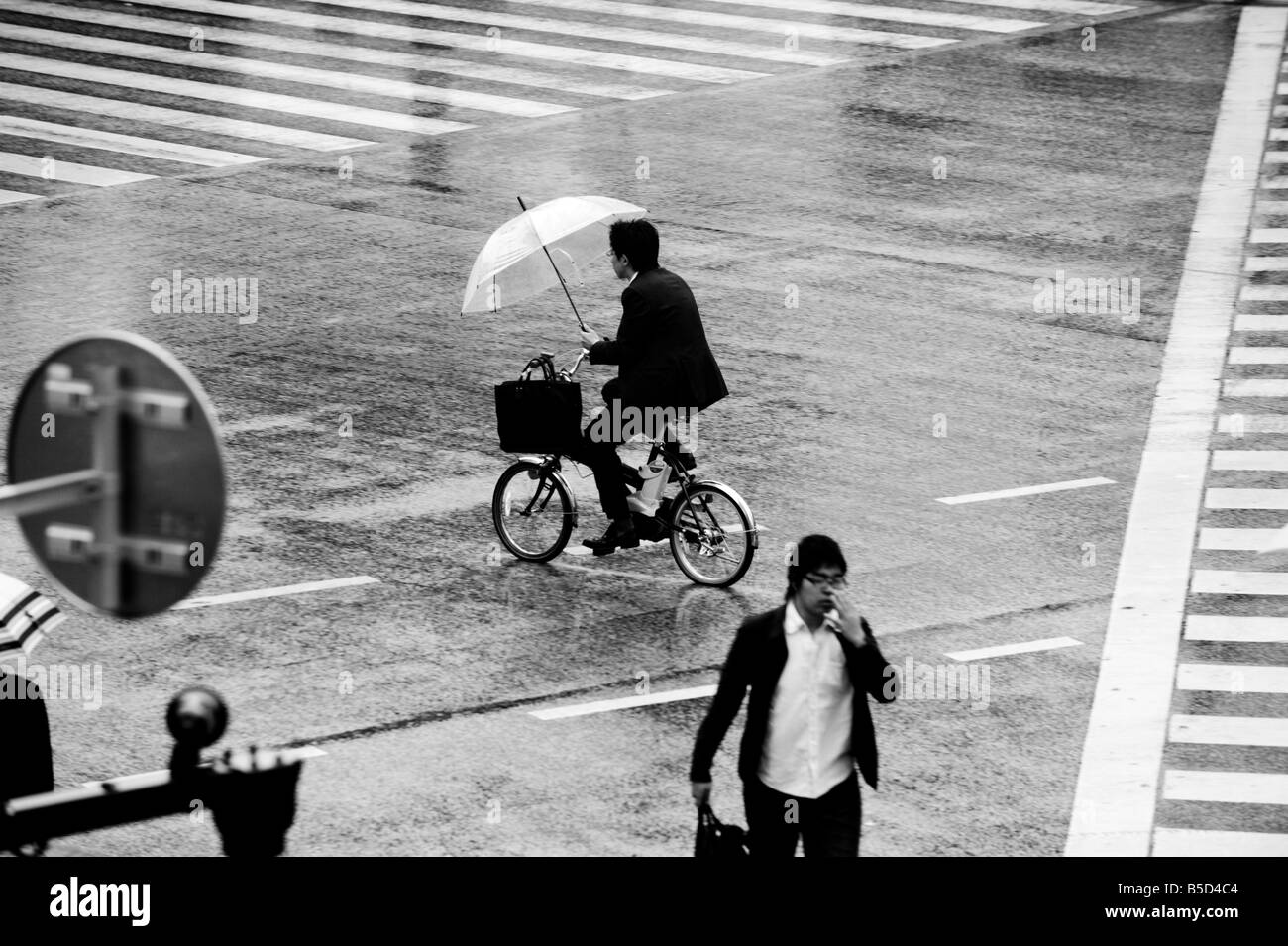 Man on bicycle with umbrella at the main crossing in The Shibuya district of Tokyo, Japan. Stock Photo