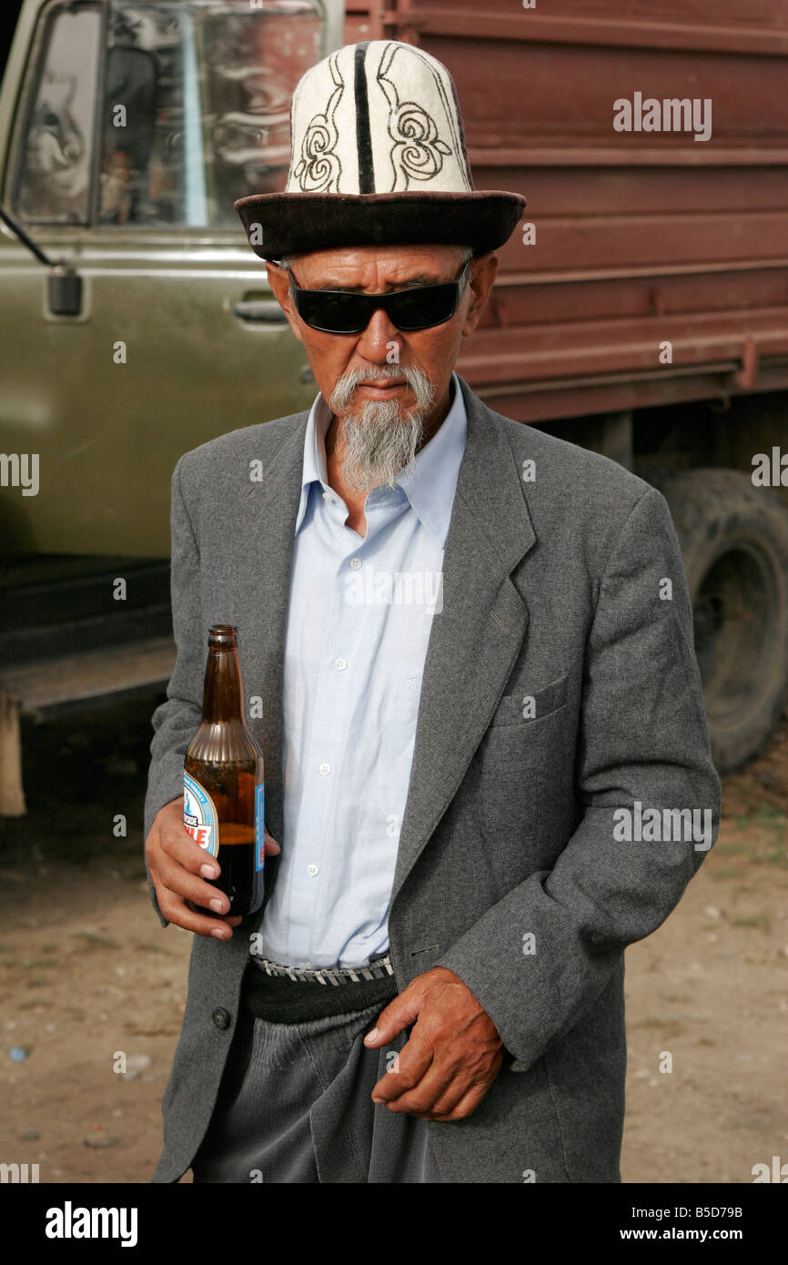 Old Kyrgyz man wearing traditional kalpak (hat) standing with the bottle of beer, Kyrgyzstan, Central Asia Stock Photo