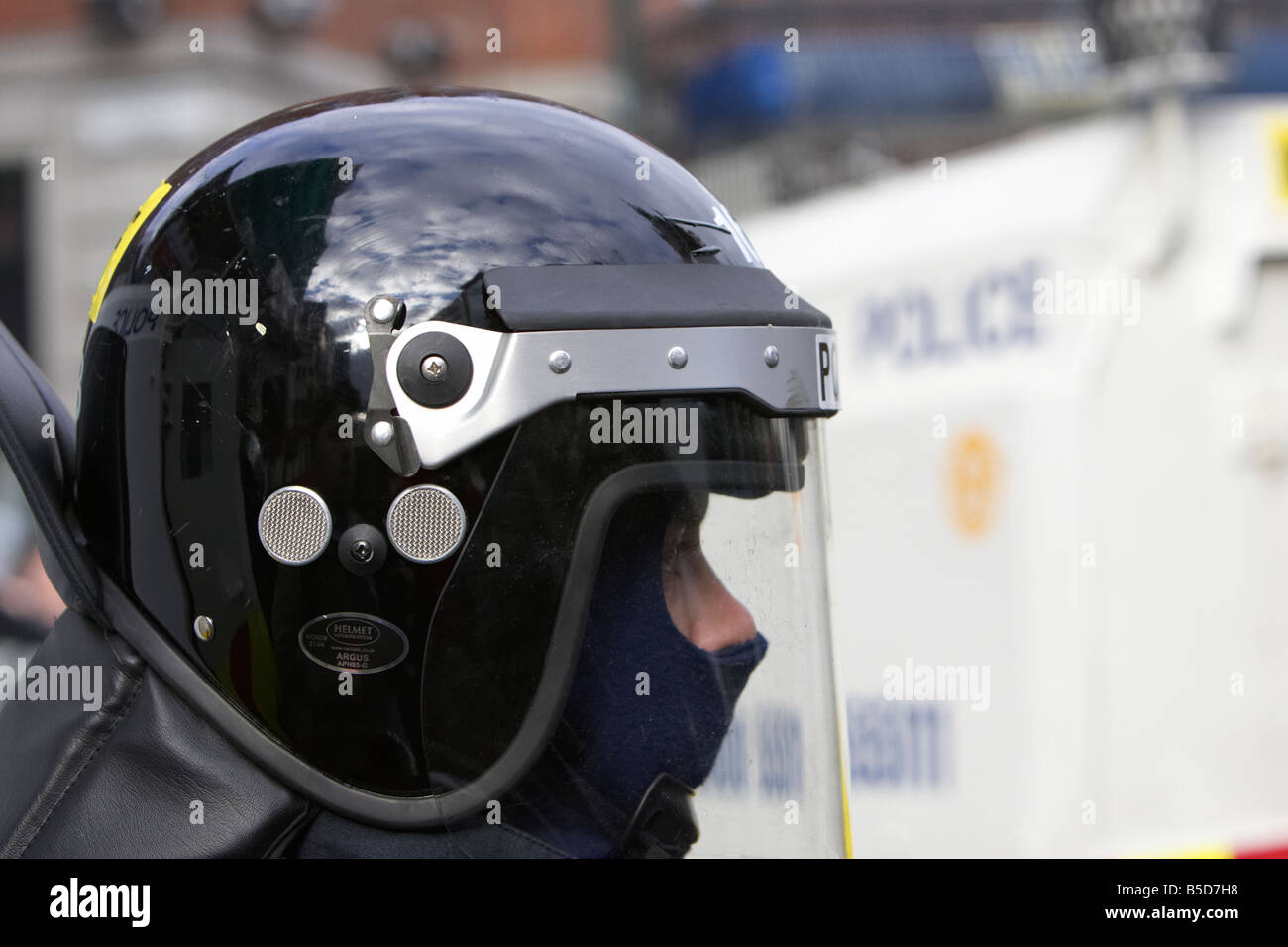 PSNI Police Service of Northern Ireland riot squad officer wearing protective helmet and visor in front of armoured landrover Stock Photo