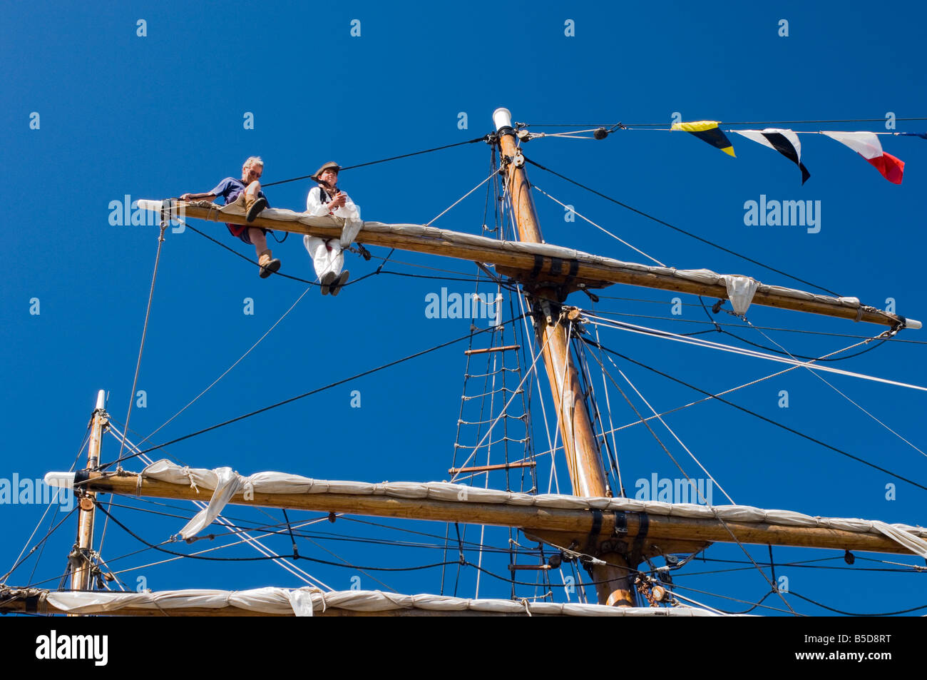Detail of main mast of tall ship with two seamen on top yard securing