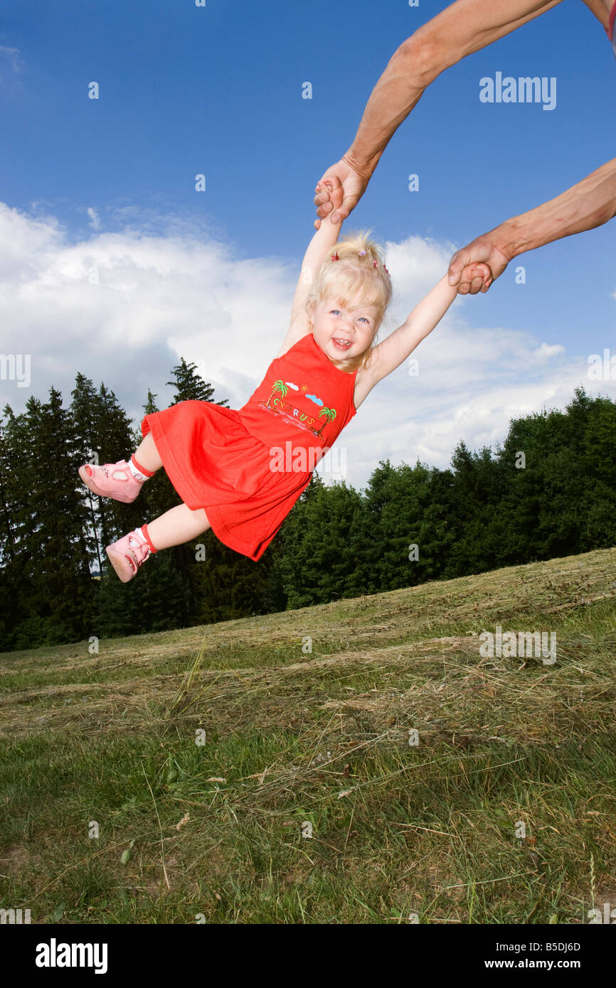 Blonde little girl being swung around, 2 years old, outside Stock Photo