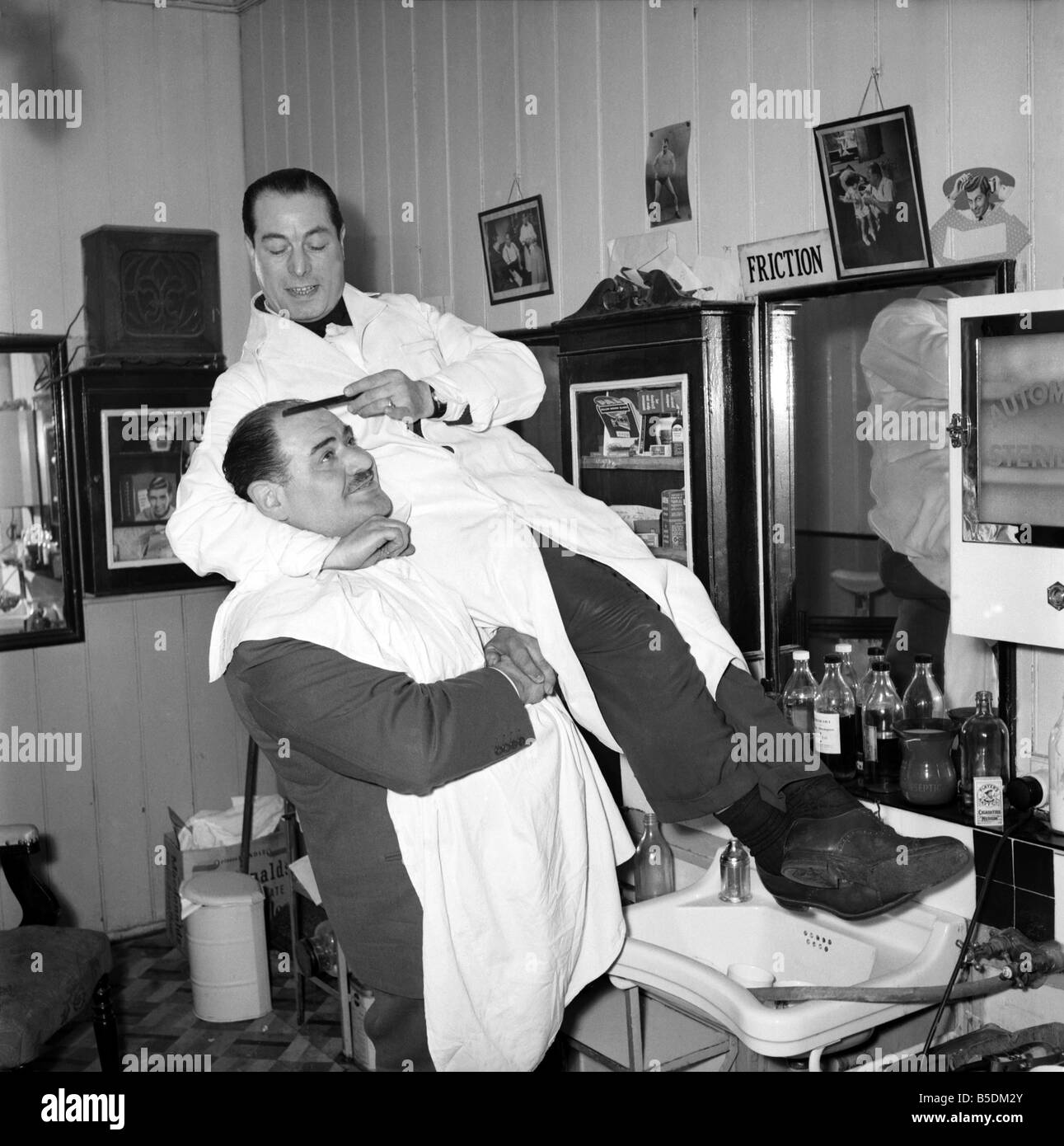 Mens Barbers Shop: Mr. Thomas the barber seen here having a joke with some of his customers. Circa 1957 Stock Photo