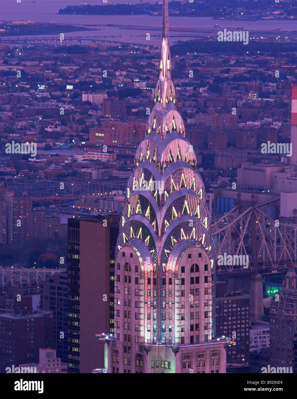 The top of the Chrysler Building illuminated in the evening with a bridge and the city of New York in the background, USA Stock Photo