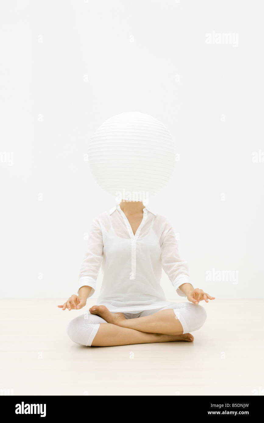 Woman sitting in lotus position, paper lantern obscuring face Stock Photo