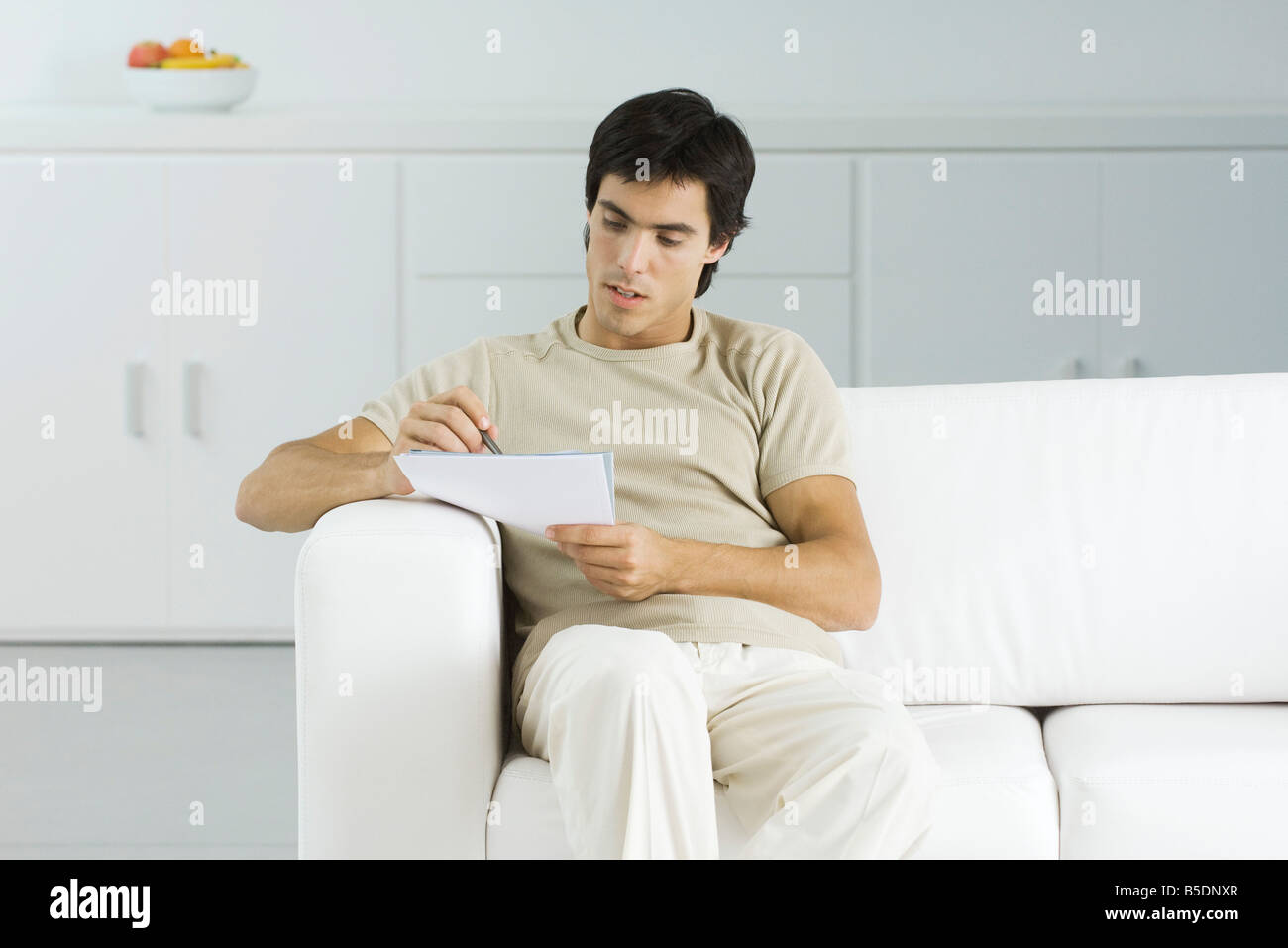 Man sitting on couch, reading document, holding pen Stock Photo