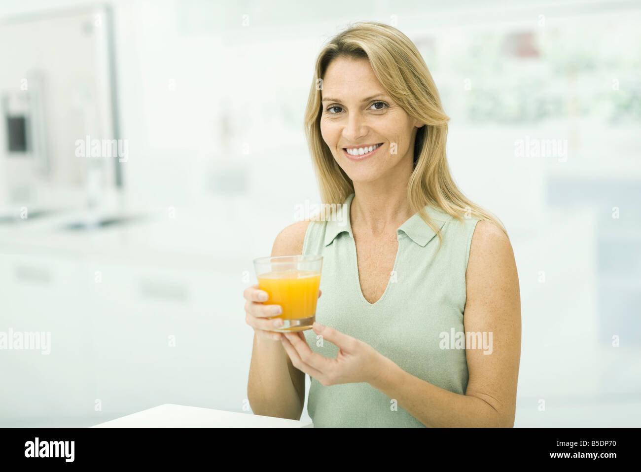 Woman holding up glass of orange juice, smiling at camera, portrait Stock Photo