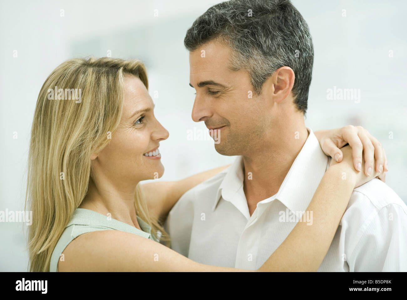 Couple smiling at each other, woman wrapping arms around man Stock
