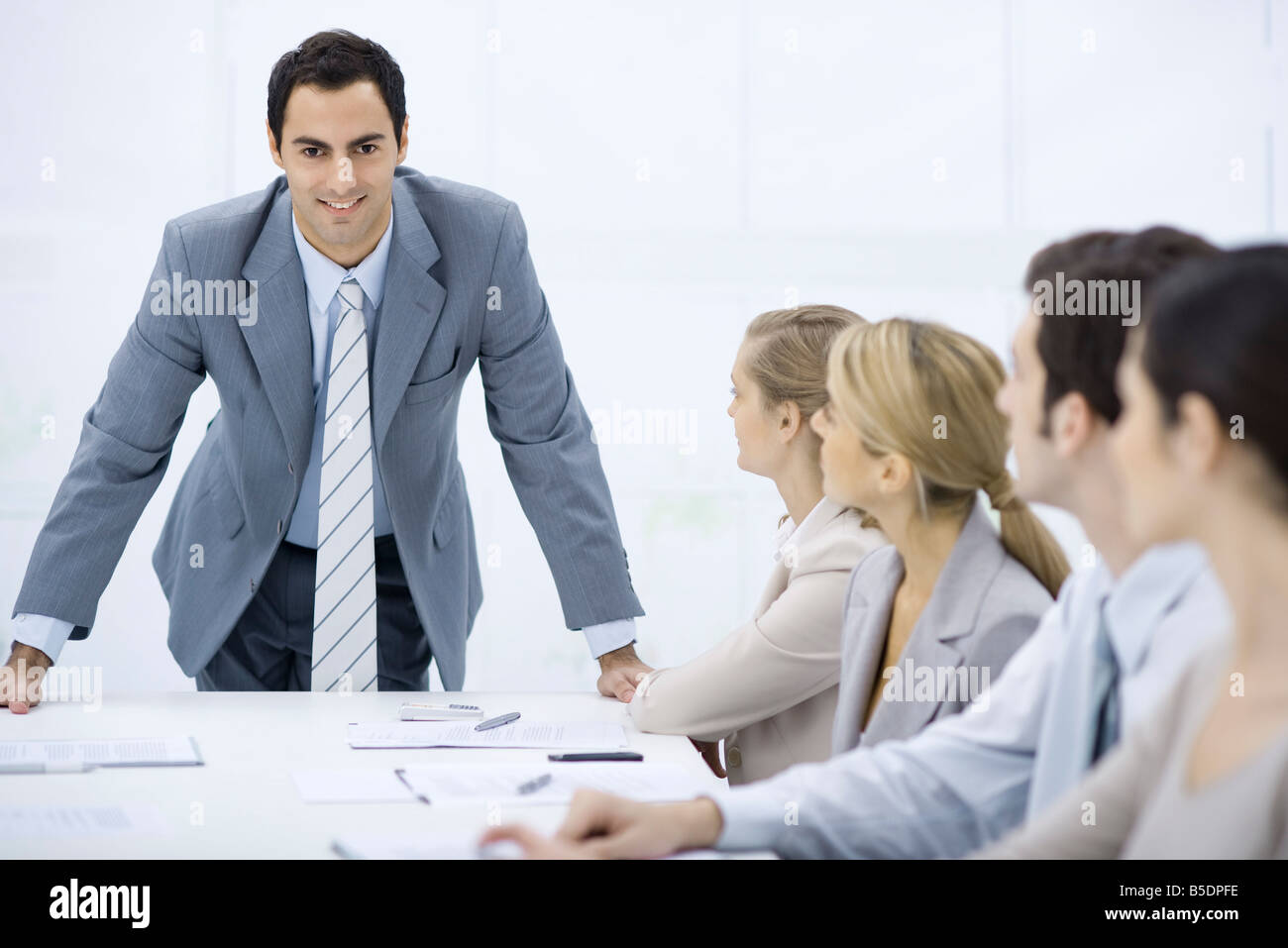 Businessman leaning over table addressing colleagues, smiling at camera Stock Photo