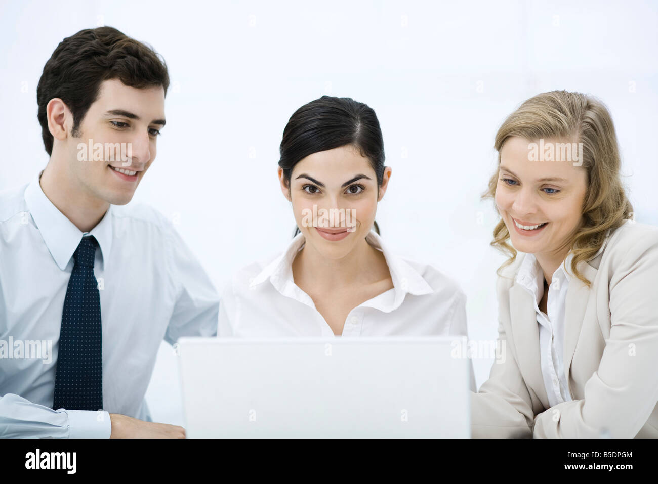 Three professionals gathered around laptop computer, woman in center smiling at camera Stock Photo