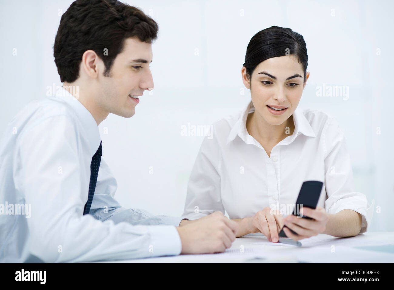 Professionals looking at cell phone together, smiling Stock Photo