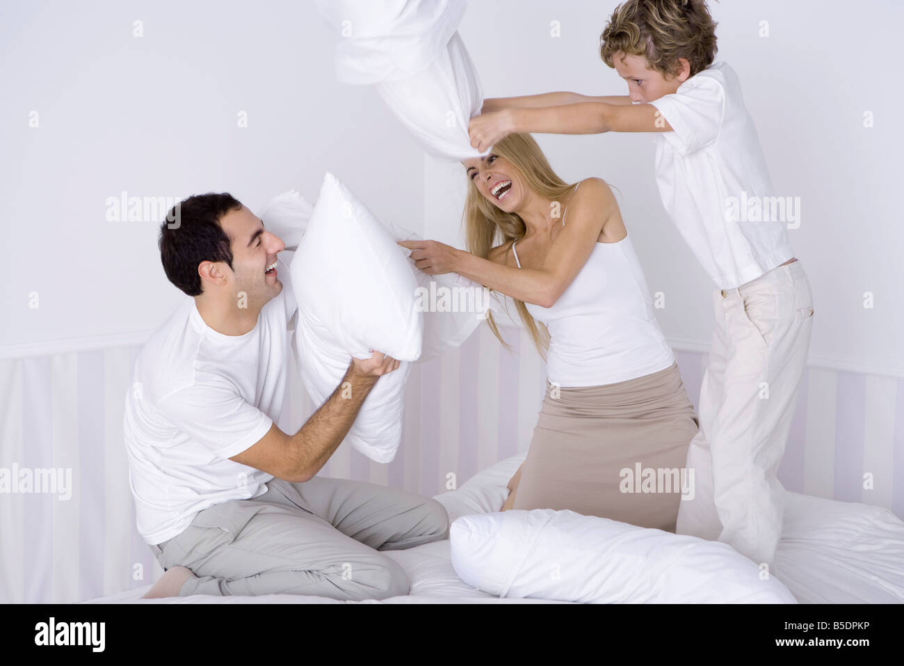 Parents and young son having pillow fight on bed Stock Photo