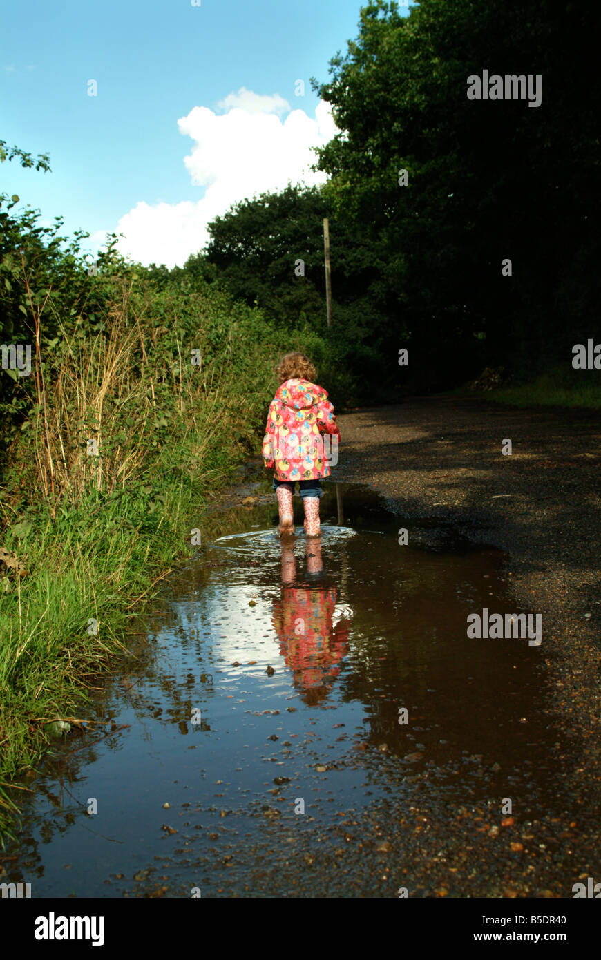 Little girl wading through a huge puddle in the countryside. Stock Photo