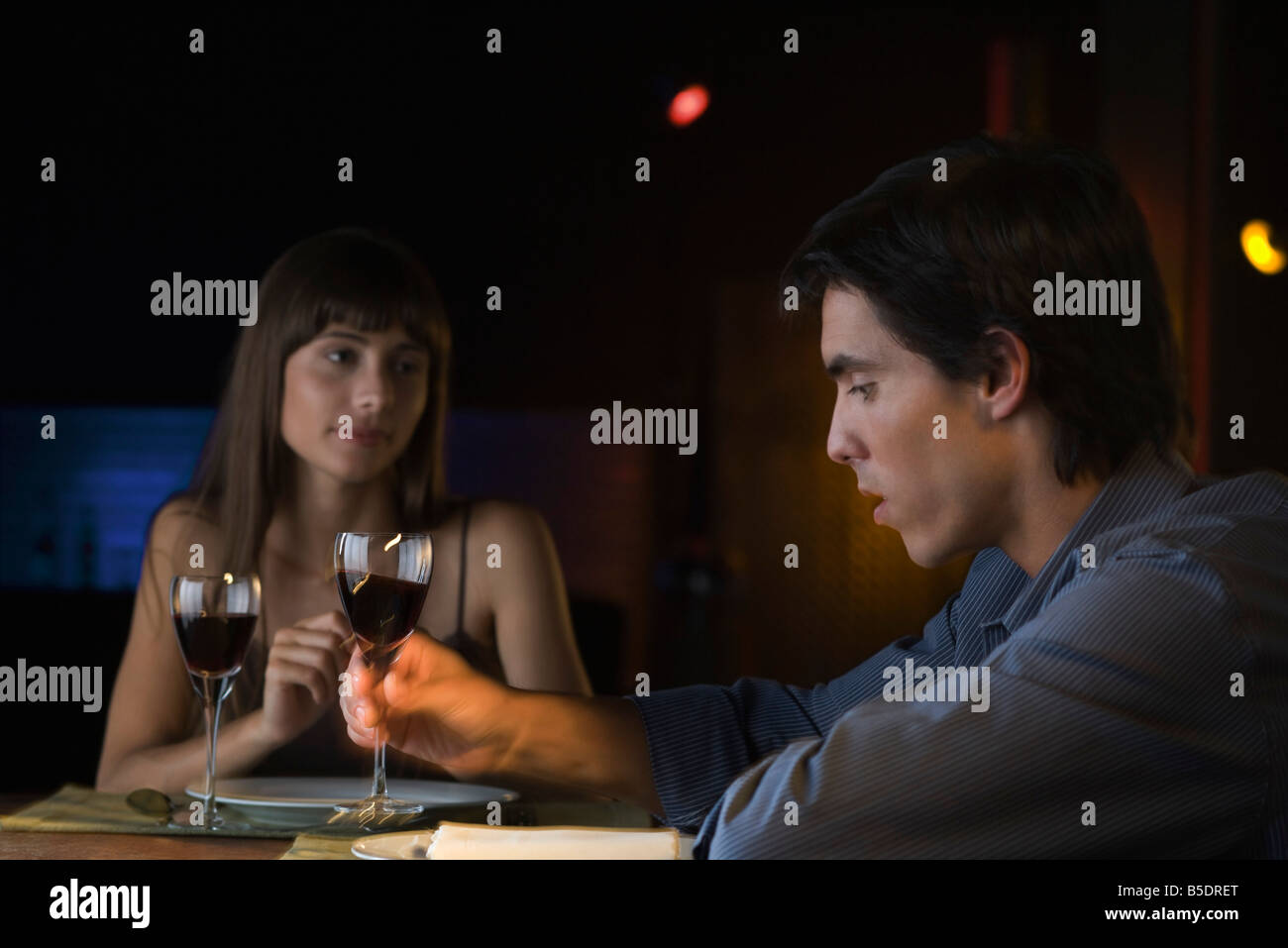 Couple having serious conversation over dinner at restaurant, man picking up glass of wine Stock Photo