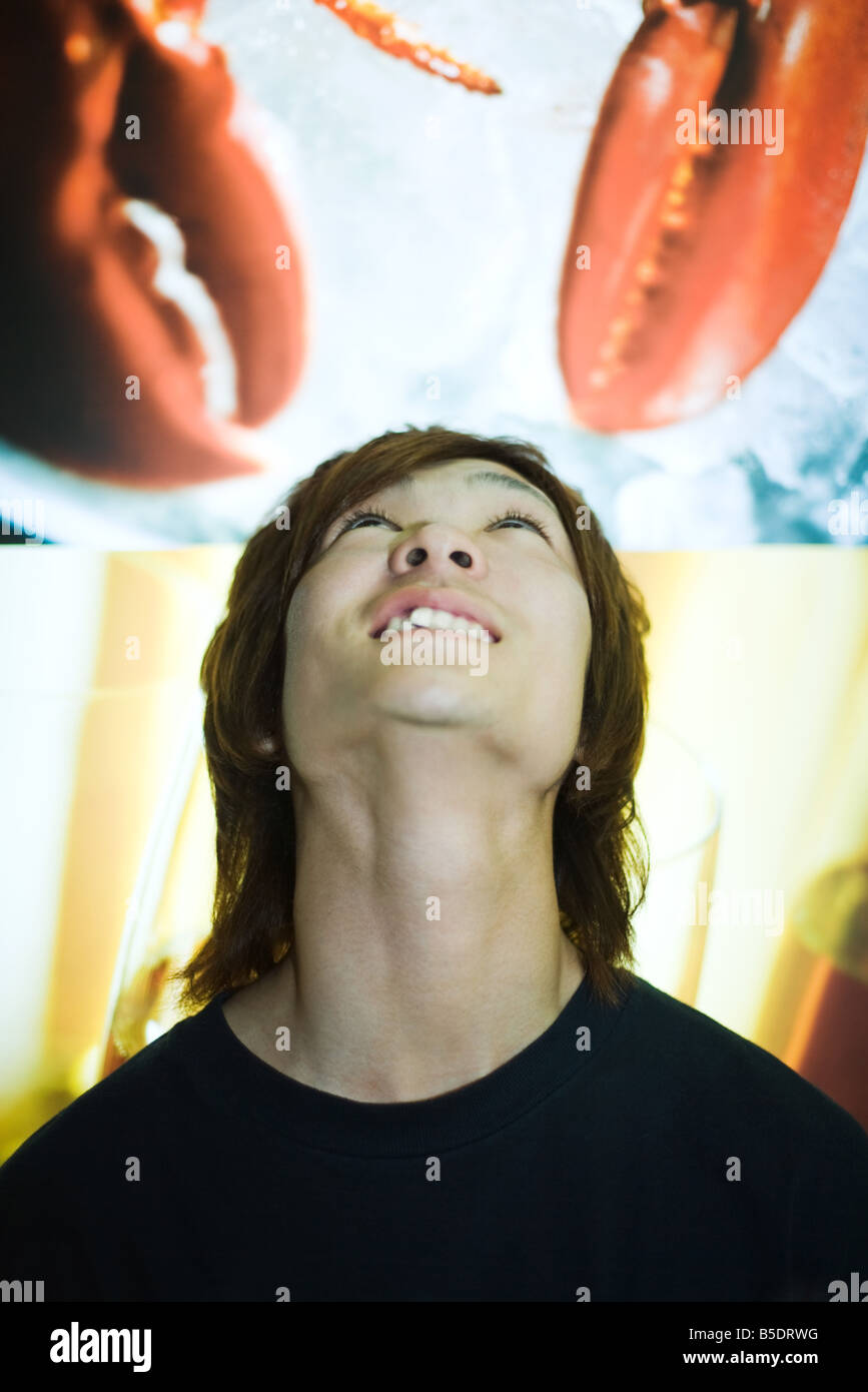 Young man standing beneath hanging poster image of lobster claws, looking up Stock Photo