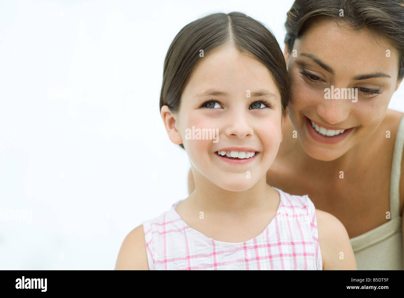 Mother leaning over daughter's shoulder, both smiling, portrait Stock