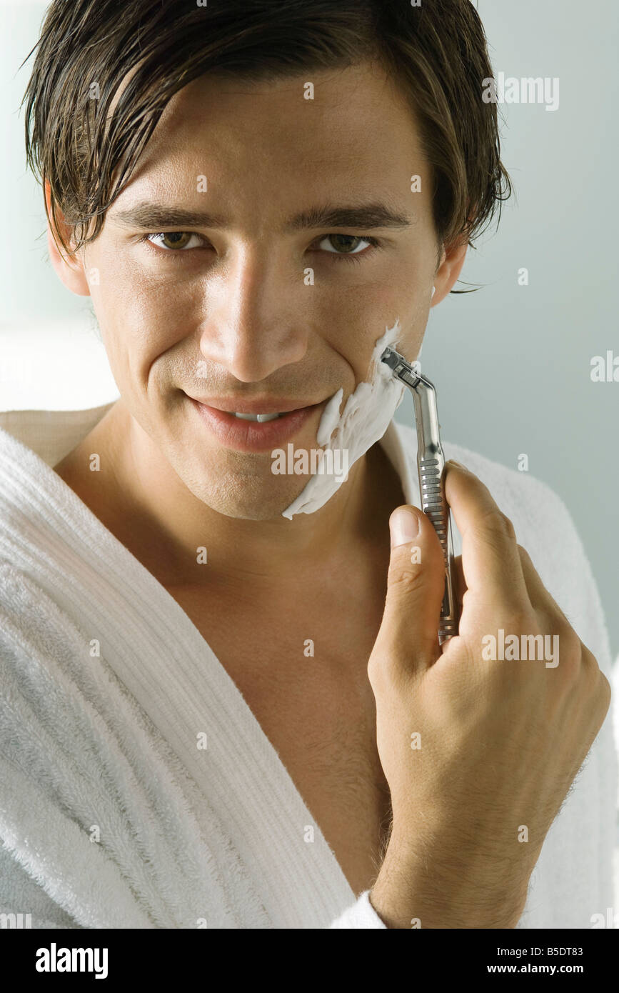 Man in bathrobe shaving, smiling at camera, close-up Stock Photo