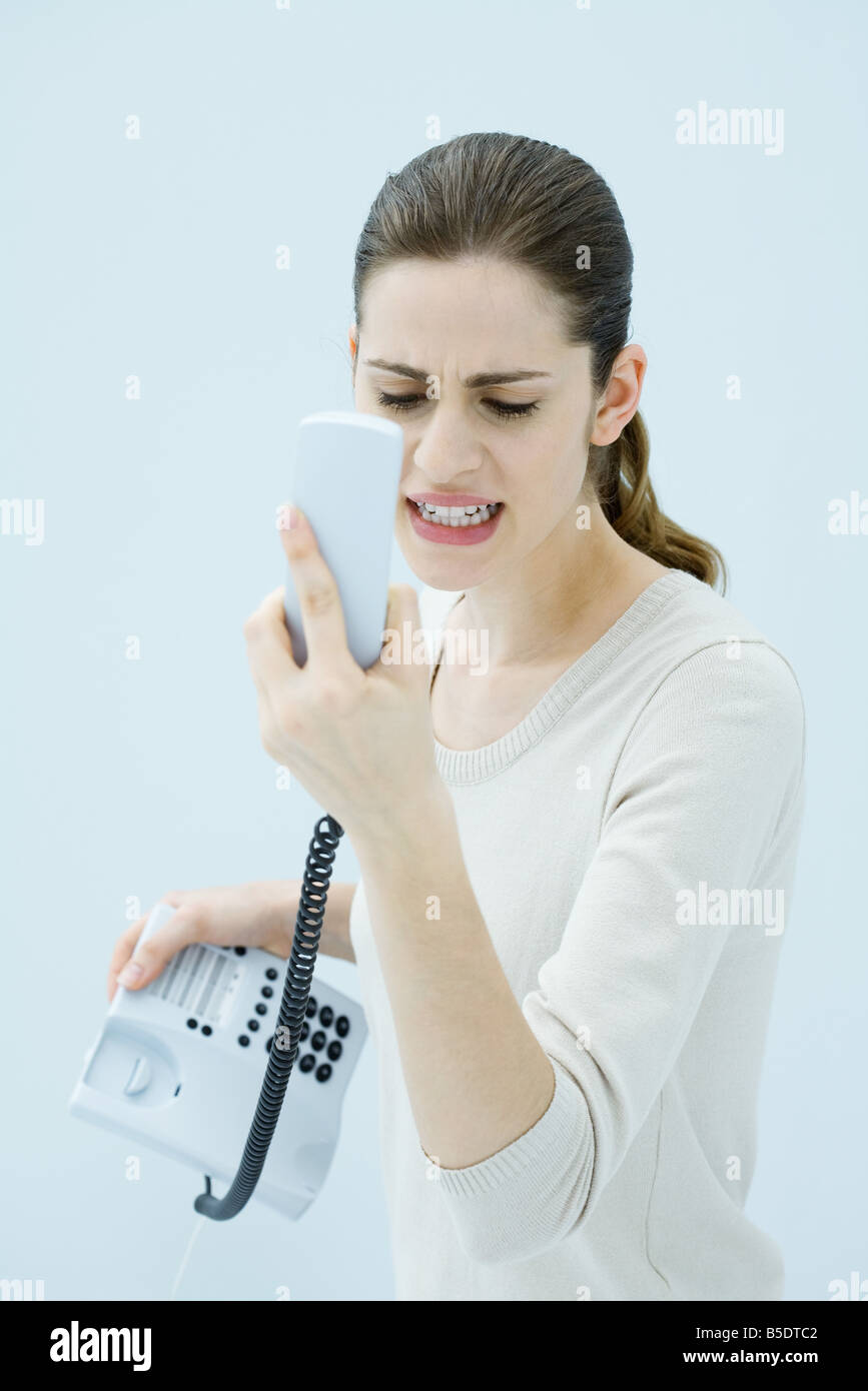 Young woman shouting at landline phone, receiver in hand Stock Photo
