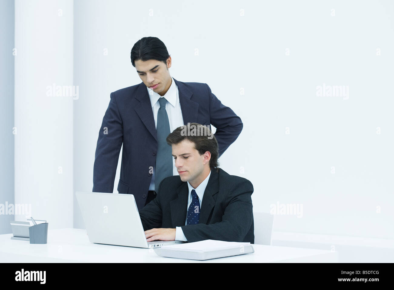 Businessman using laptop computer at desk, colleague watching over his shoulder Stock Photo