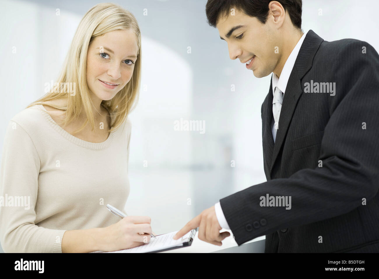 Businessman holding out clipboard, woman writing on document and smiling at camera Stock Photo