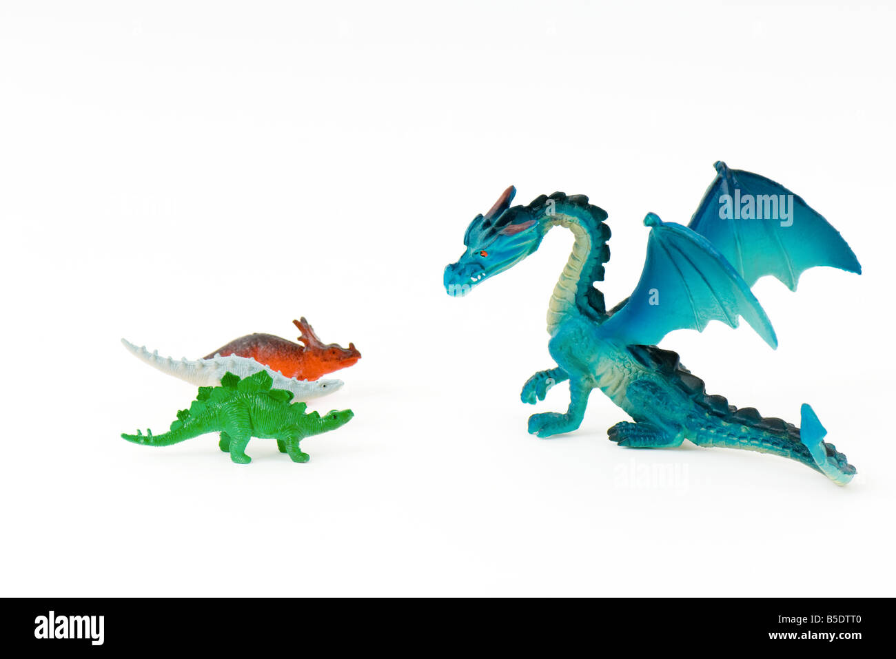 Toy dragon facing three small toy dinosaurs Stock Photo