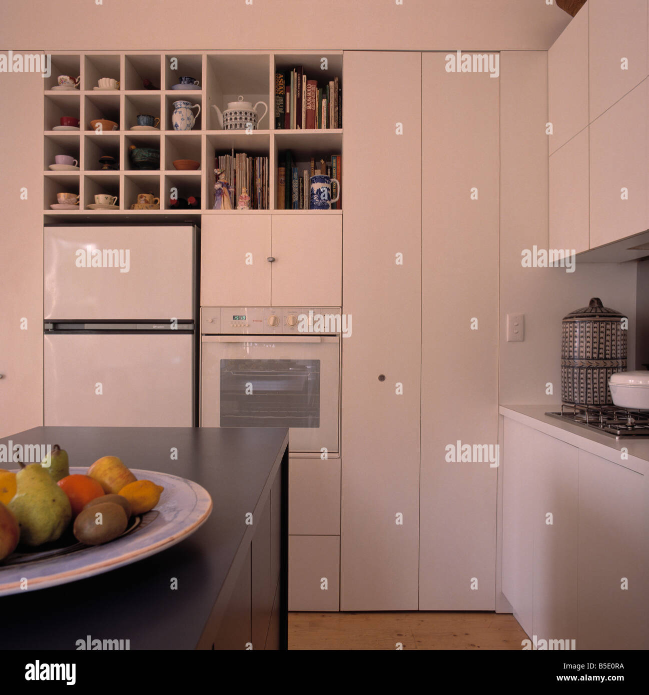 Cube shelves above fridge freezer and eye-level in modern white kitchen  with bowl of fruit on grey island unit Stock Photo - Alamy