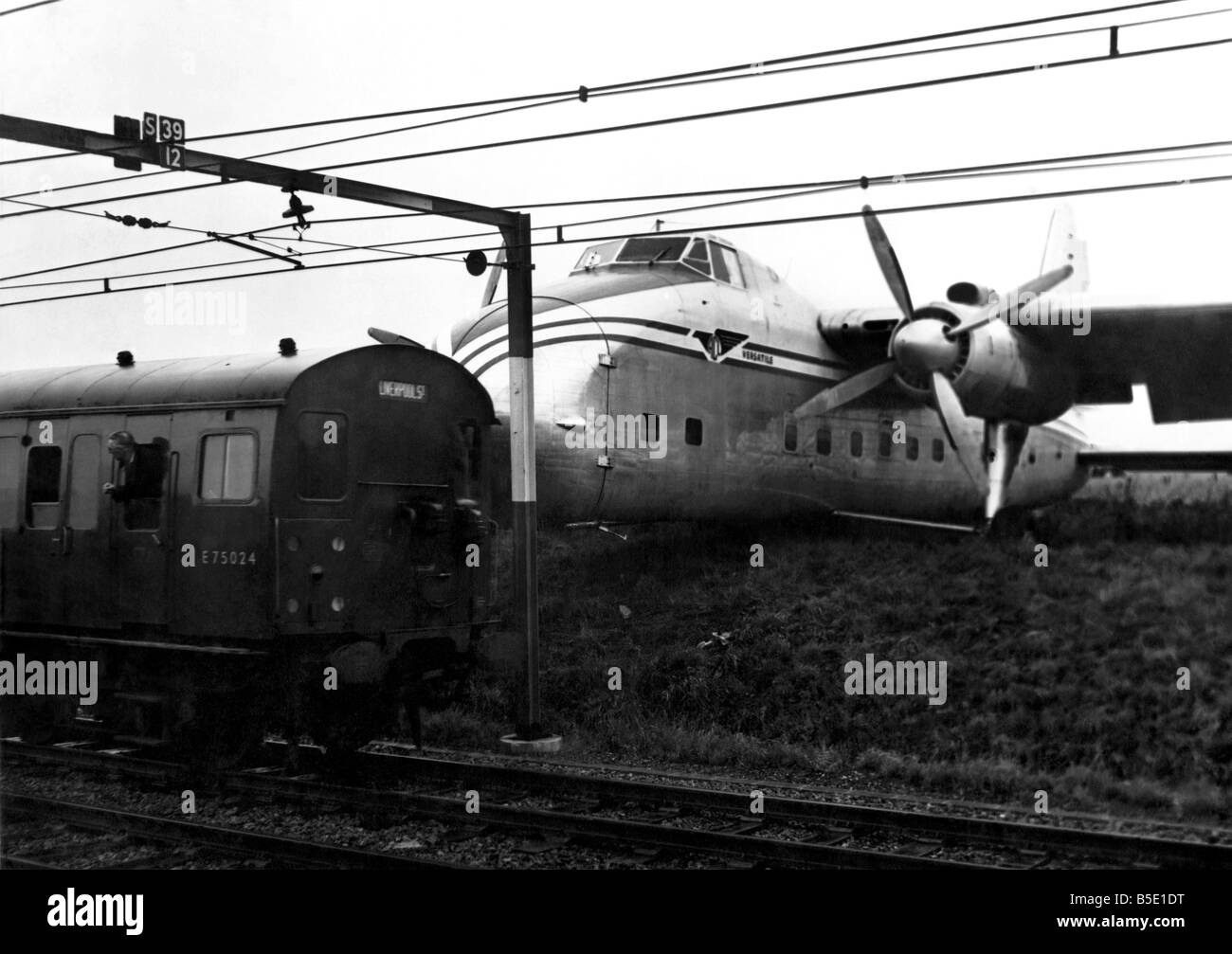 This Bristol Freighter airliner overshot the runway when it was landing at Southend Airport. Then it crashed through a fence and stopped - just a few feet from an electric railway line. Overhead are high tension cables carrying a load of 1,500 volts. None of the thirteen people in the plane were hurt and no trains were near when the crashed happened. The plane, belonging to Air Charter, Ltd. was flying from Calais, France, with ten passengers and a crew. There were also three cars aboard. They were all given a shaking when the plane crashed Stock Photo