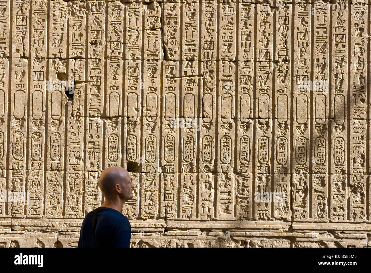 Tourist Looking at a Wall of Hieroglyphs at the Temple of Horus in Edfu Egypt Stock Photo