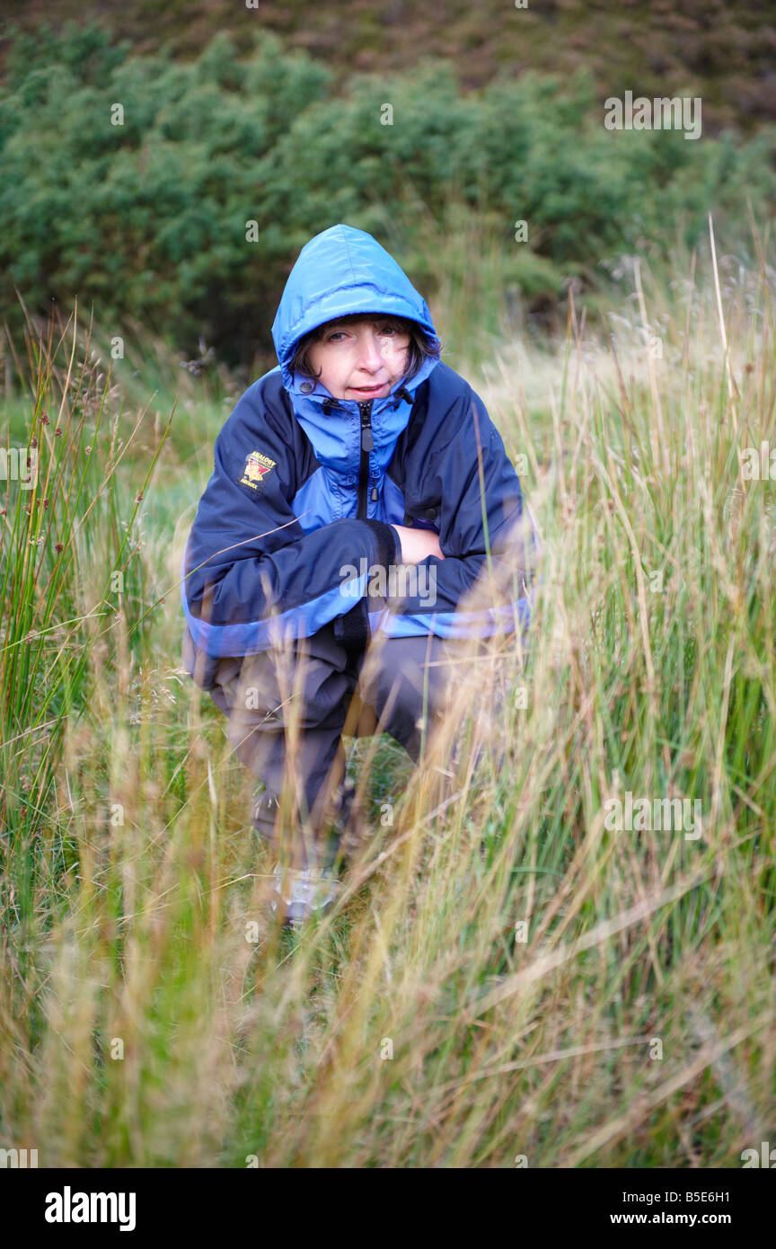 Woman squatting urinating in the wilds hiding behind grass Scotland UK