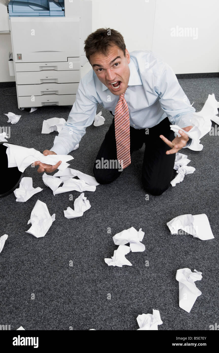 Businessman kneeling among slips of paper, gesturing in despair Stock