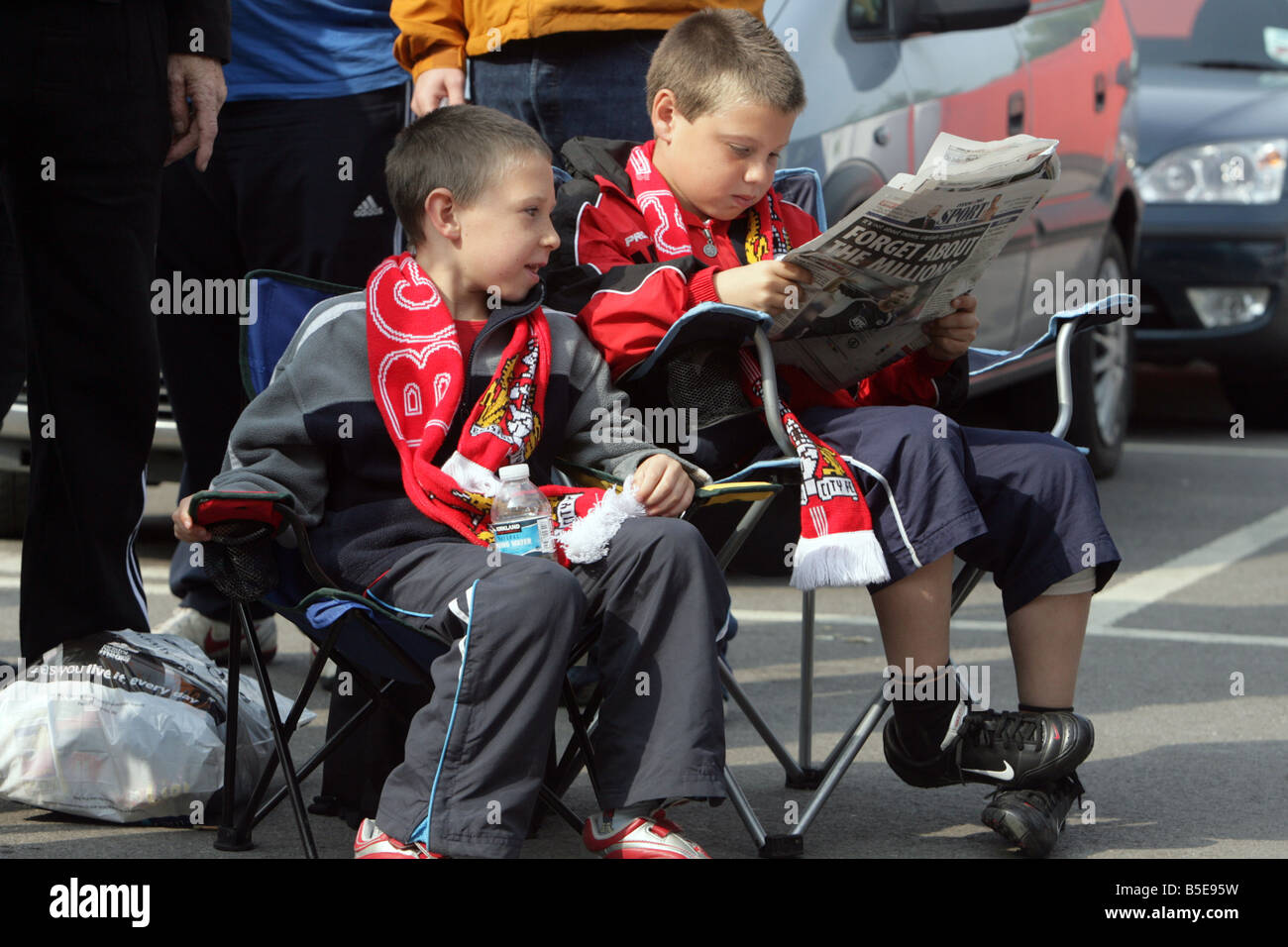 two young Bristol City football fans sit in chairs in a que for football tickets, one boy reads a newpaper. Stock Photo