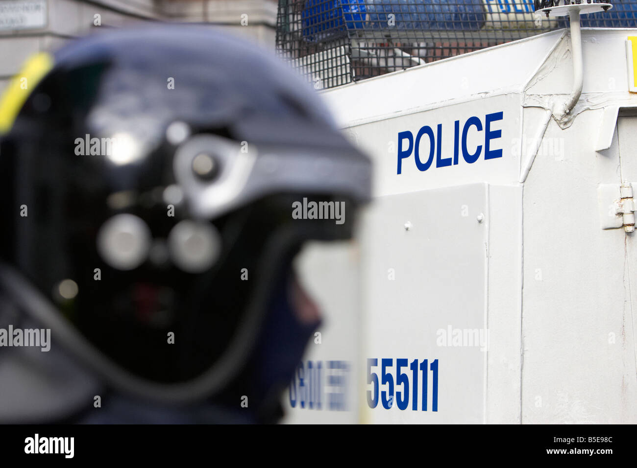 PSNI Police Service of Northern Ireland riot squad officer wearing protective helmet and visor in front of armoured landrover Stock Photo