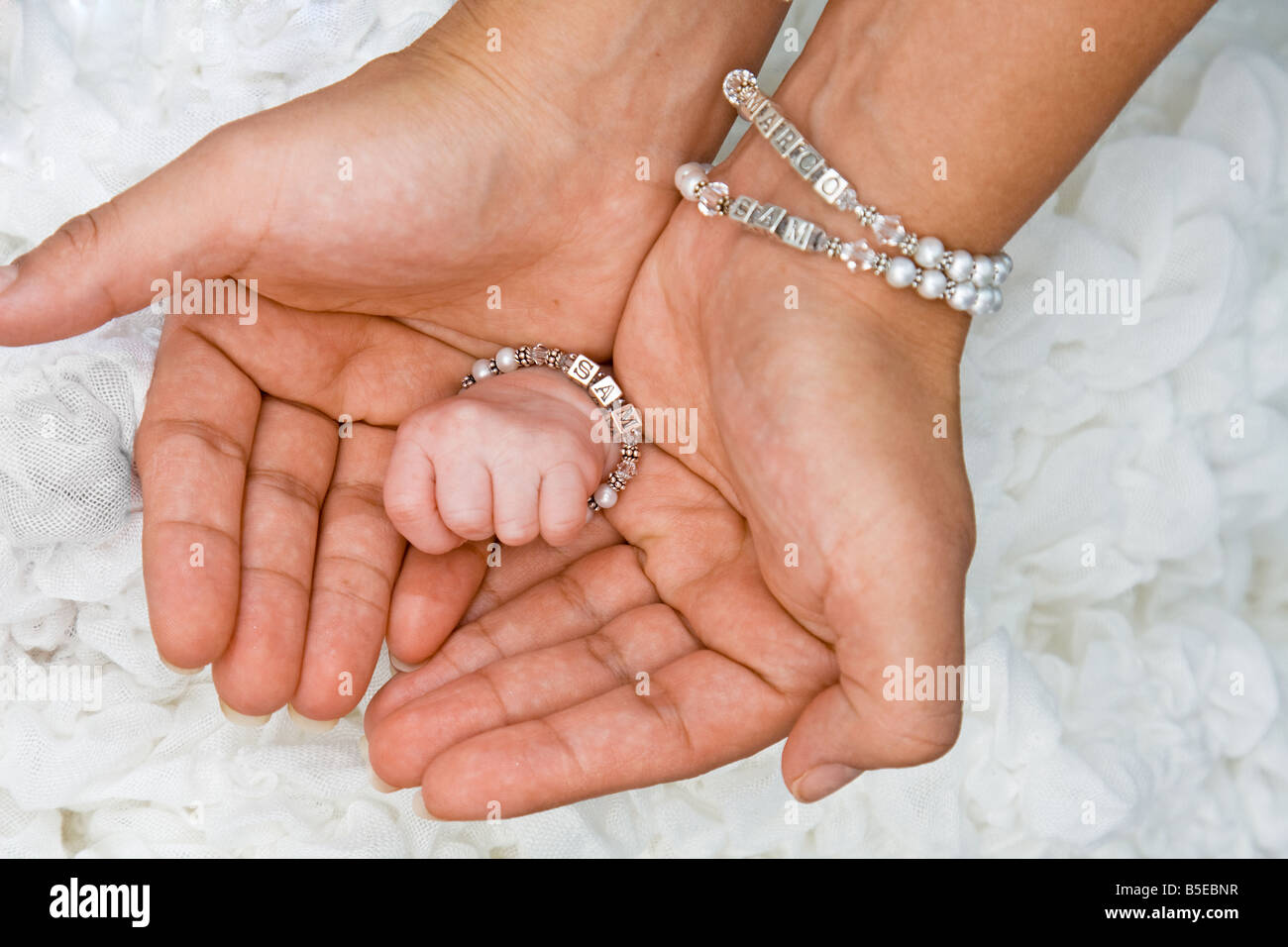 Cute small baby hand inside 2 female adult hands with bracelets Stock Photo