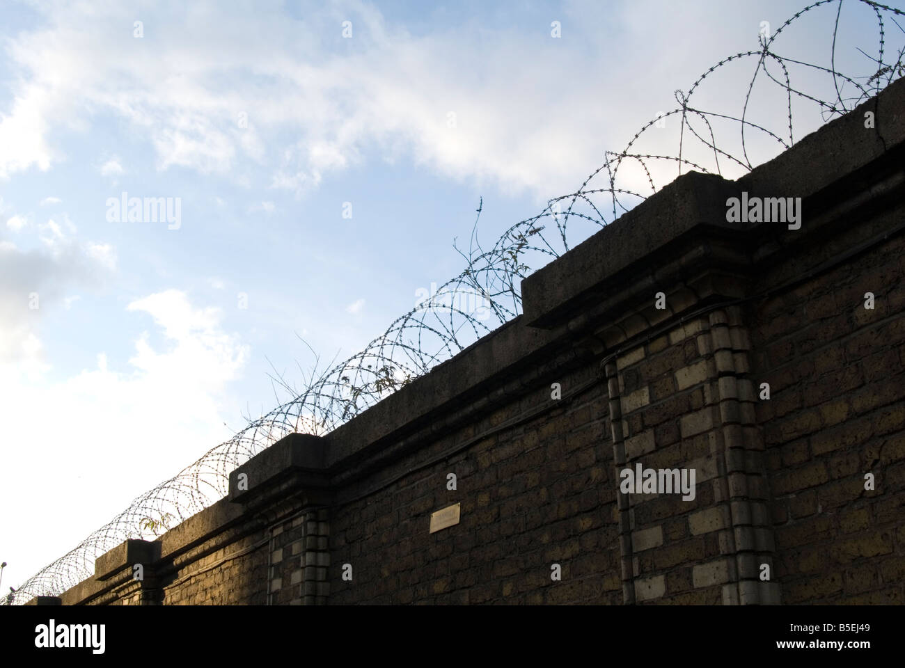 An image of a high brick wall with barbed wire spiraling accross the ...