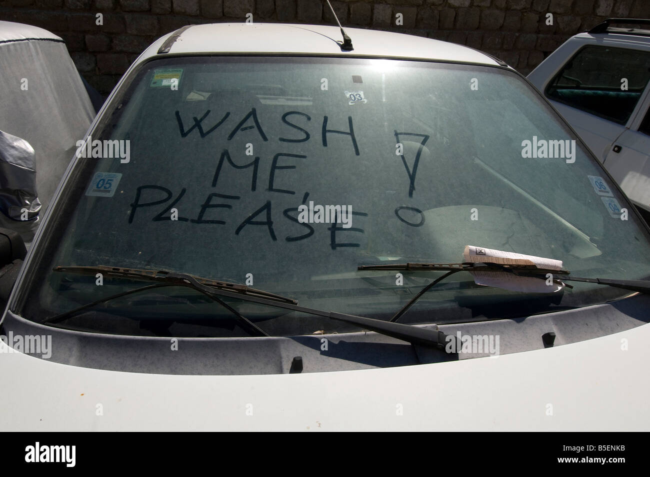 A Wash Me Please inscription plea written on the filthy windowscreen of a dirty car Stock Photo