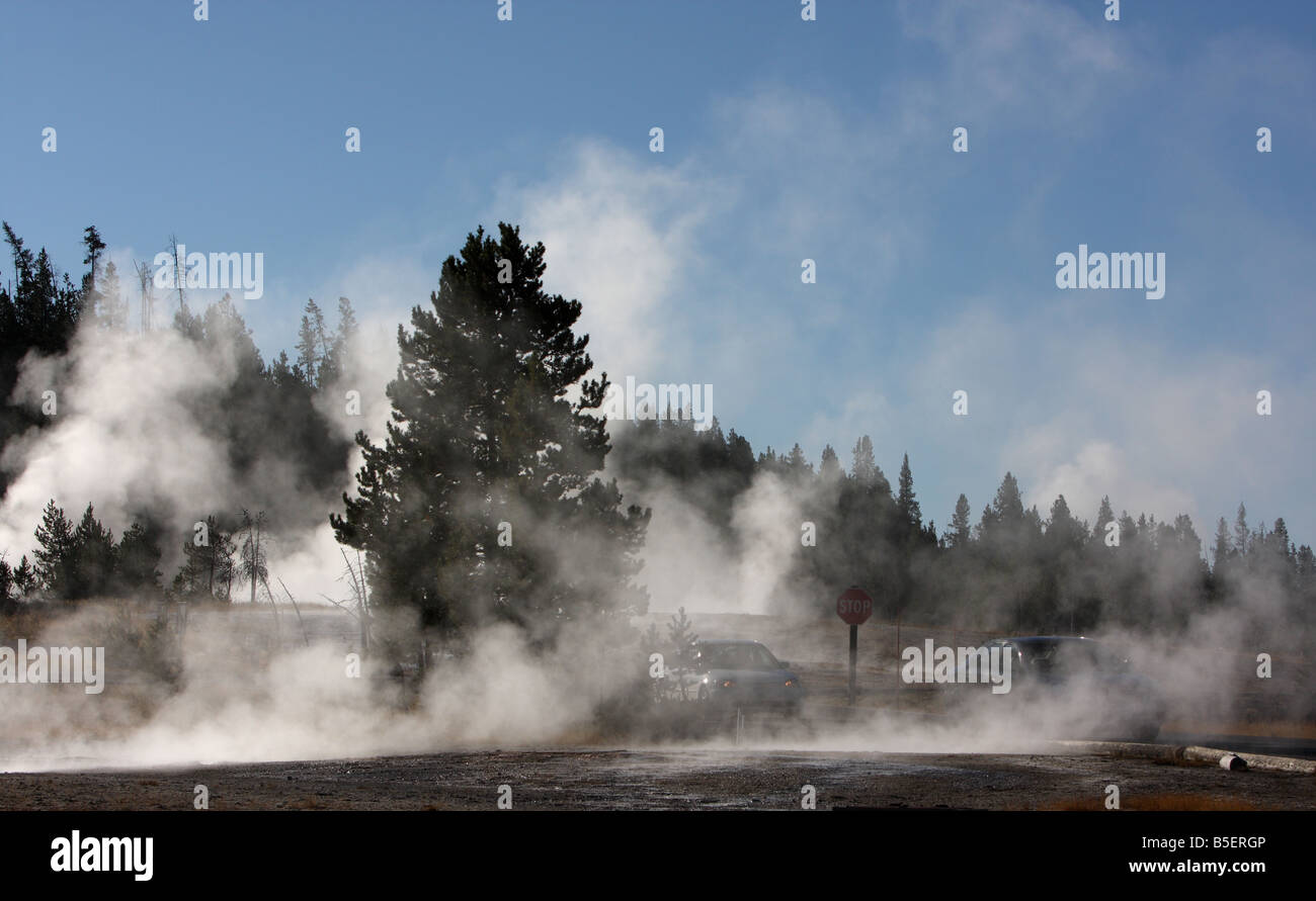 Cars driving past steaming thermal features at Yellowstone National Park, Wyoming Stock Photo