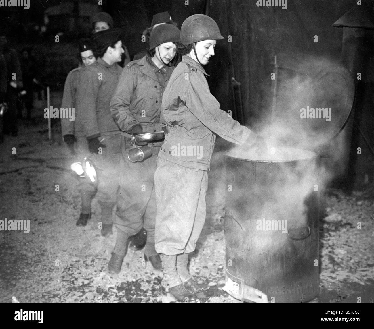 Women of a US Army nursing unit queue up with plates and mugs while camping in Wales to receive their food which is cooking in a giant tin during the Second World War All the equipment they need including operating theatres x ray and dental departments is at the camp February 1944 Stock Photo