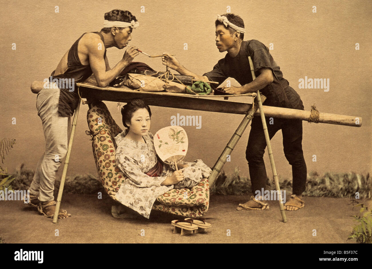 19th century hand-tinted Japanese Albumen print of woman and two porters smoking (by Baron von Stillfried or Felice Beato). Stock Photo