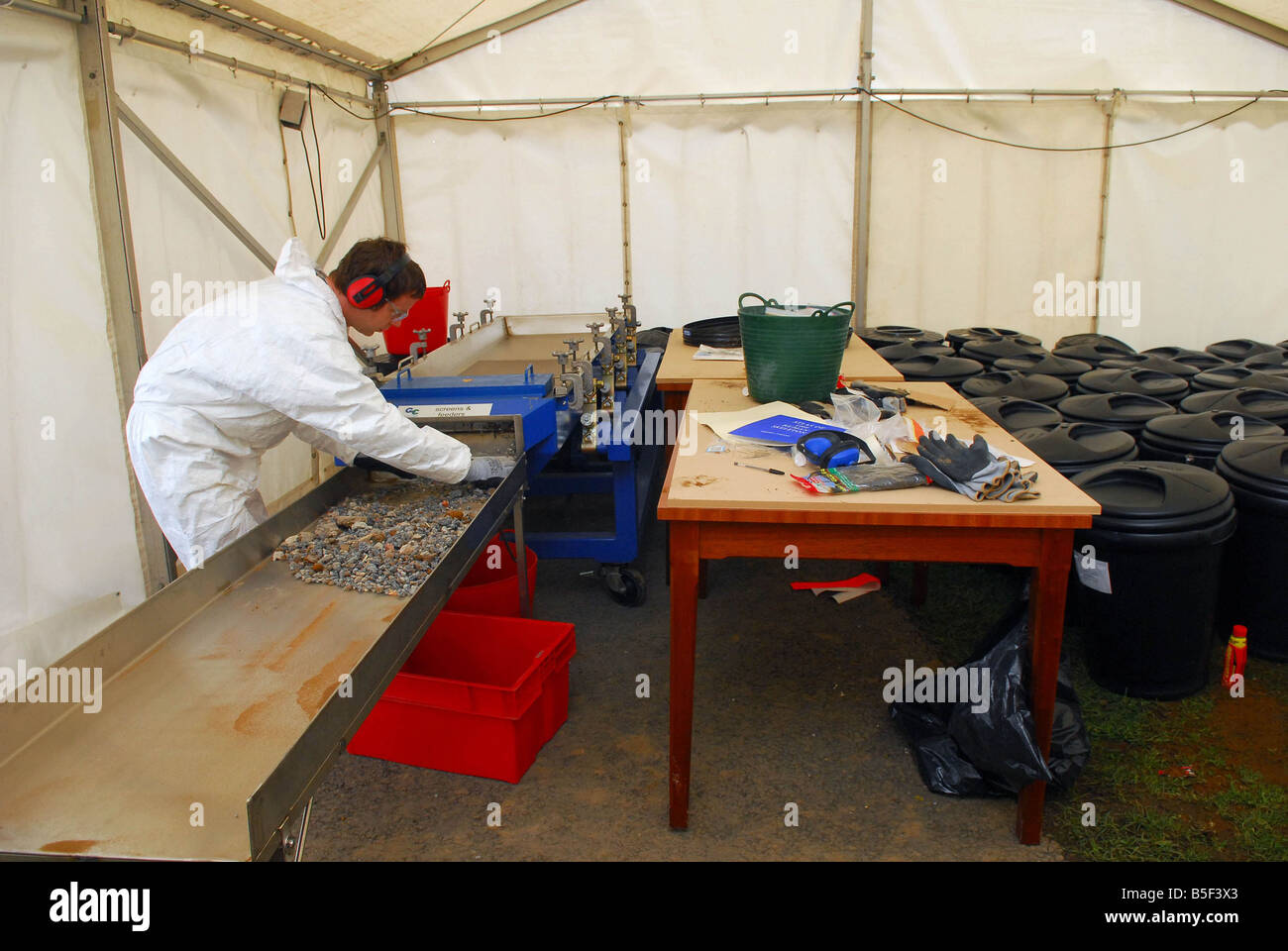 Forensic officer in tent sifts through rubble from a room in the Hostel Haut De La Garenne looking for possible human remains Stock Photo