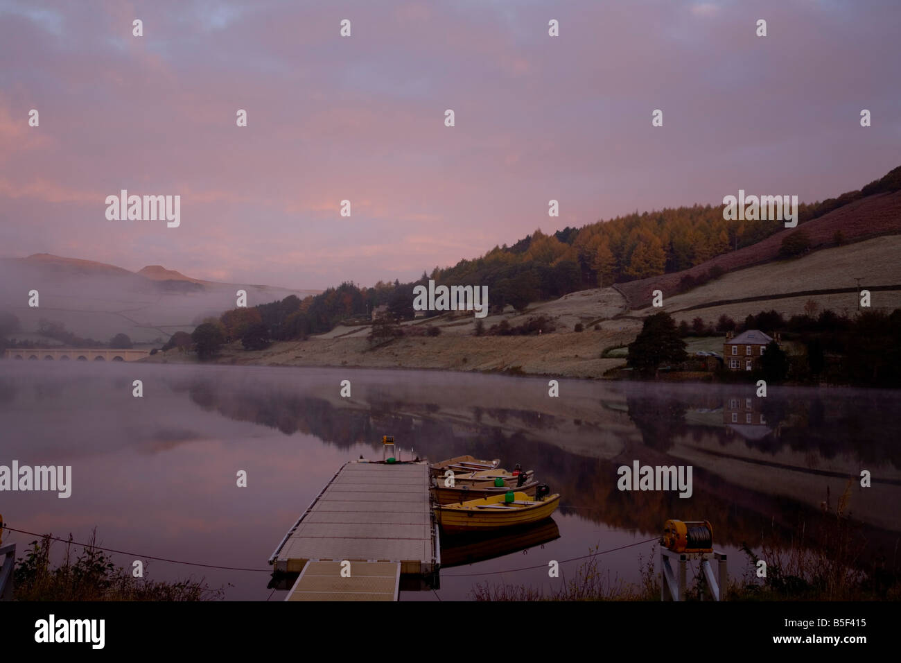 Misty sunrise over Ladybower Dam. Boats moored to a pontoon many reflections in the calm water. Ashopton viaduct in background. Stock Photo