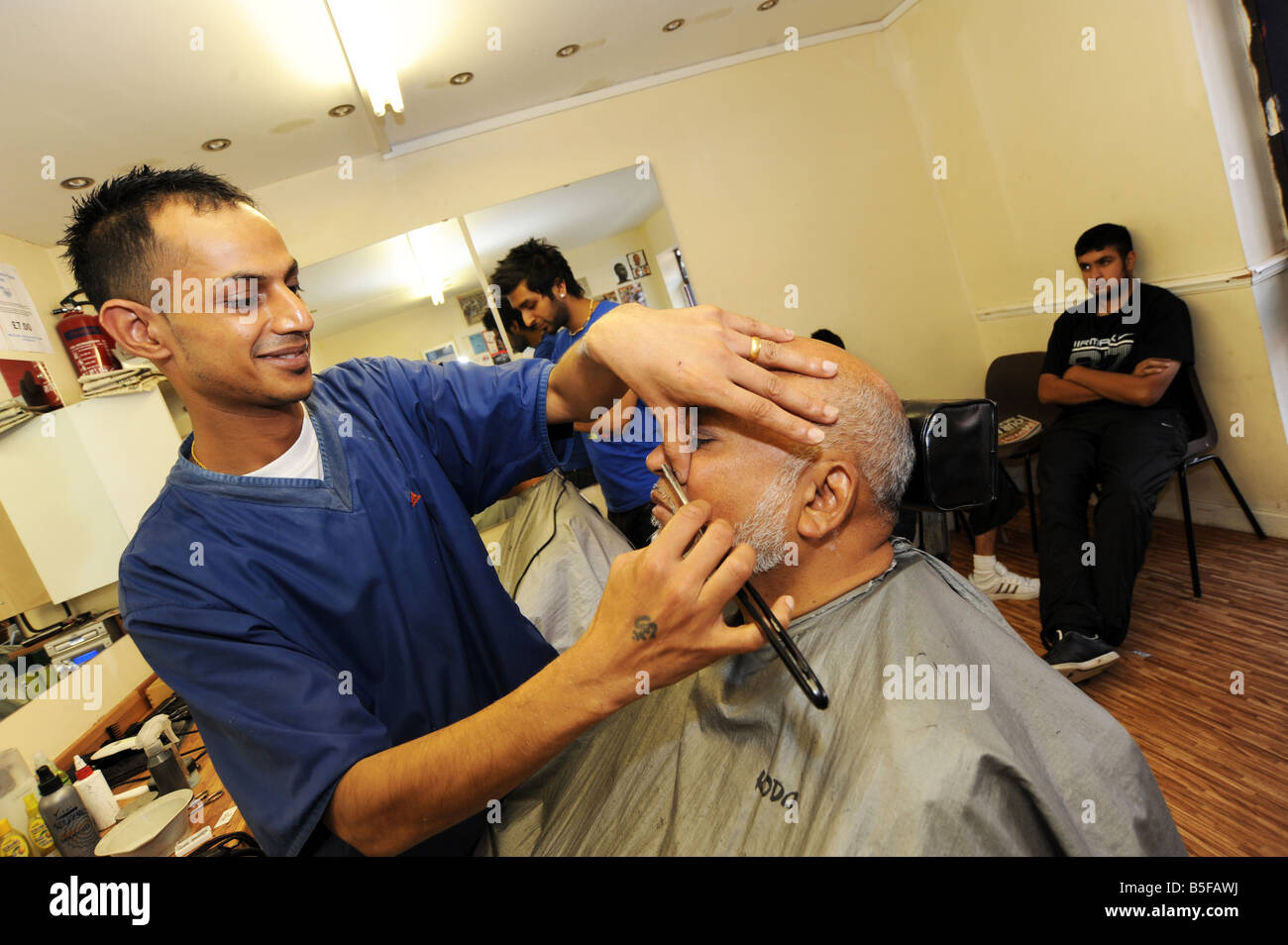 A man has a wet cut throat shave in a busy barbershop in Bolton, Greater Manchester UK Stock Photo