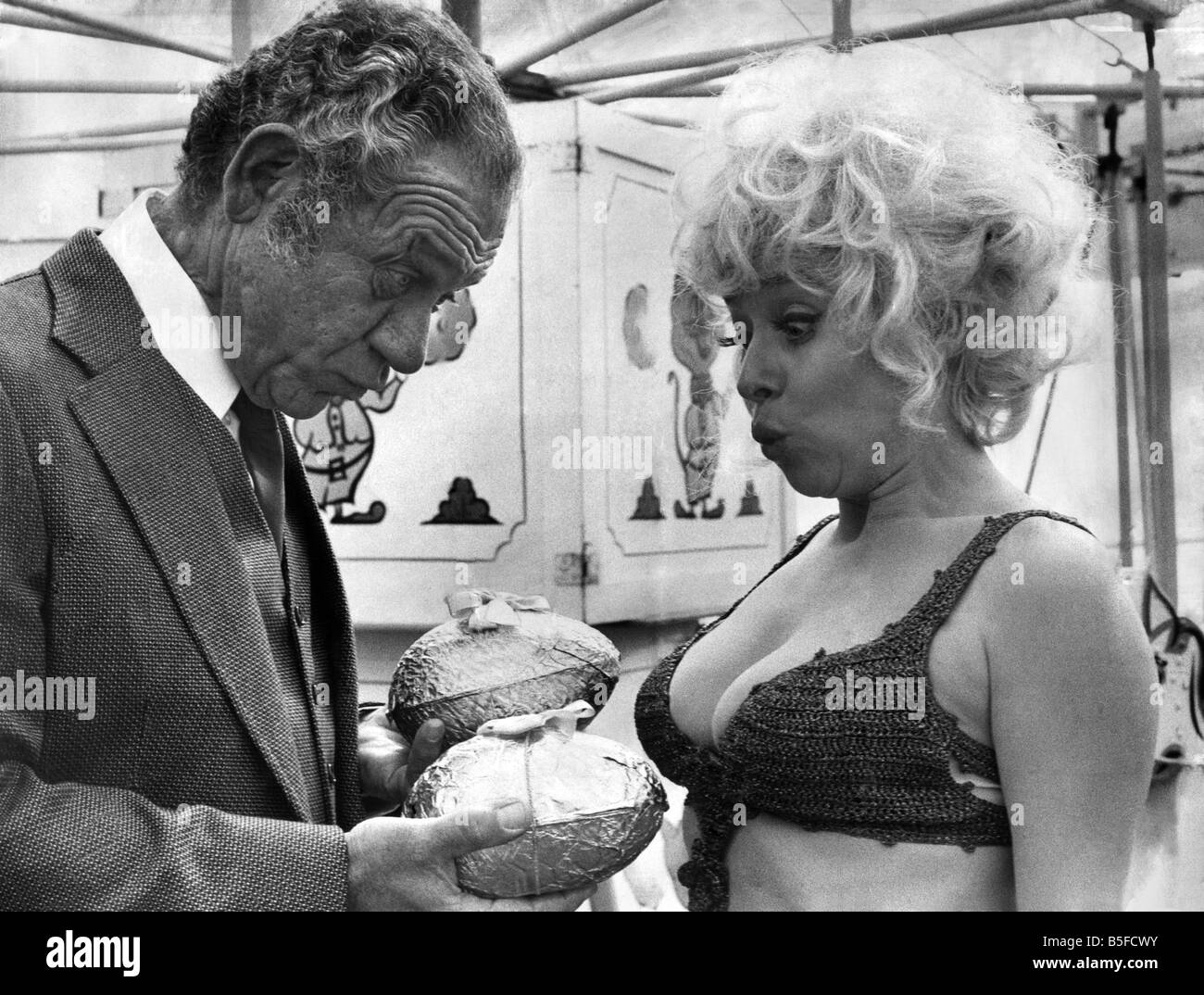 A break in filming of “Carry On Girls” Sid James in true Carry on tradition presents Barbara Windsor with two Easter eggs. 1973 Stock Photo