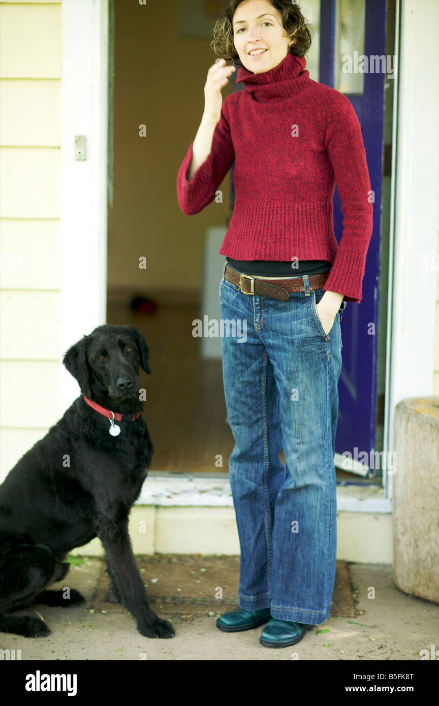 Lanky woman in her forties stands in the threshold with her black labradoodle puppy hybrid pooch. Cute, sweet, and allergy free! Stock Photo