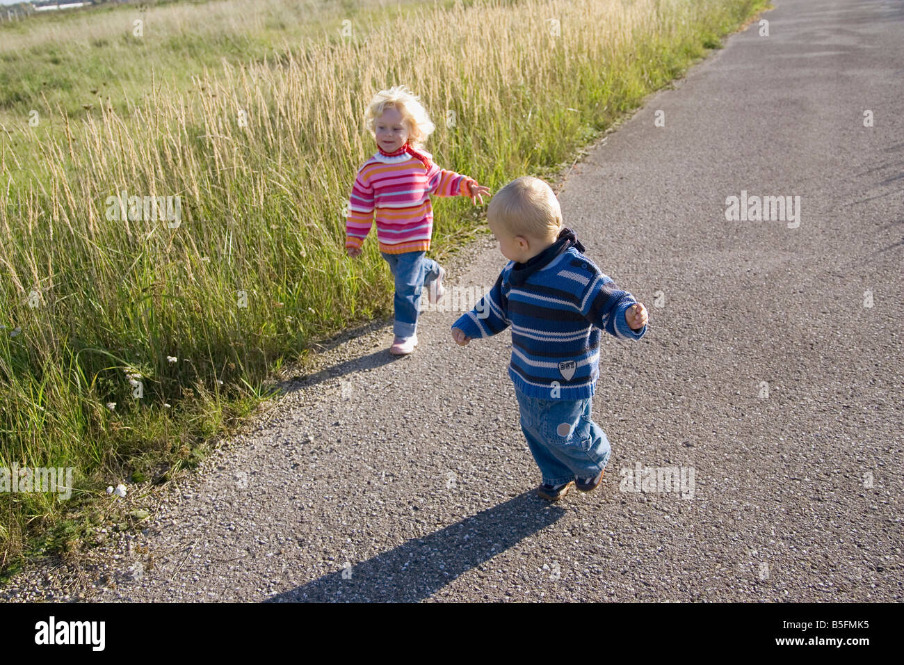 Little girl (2-3) and boy (1-2) running across path Stock Photo